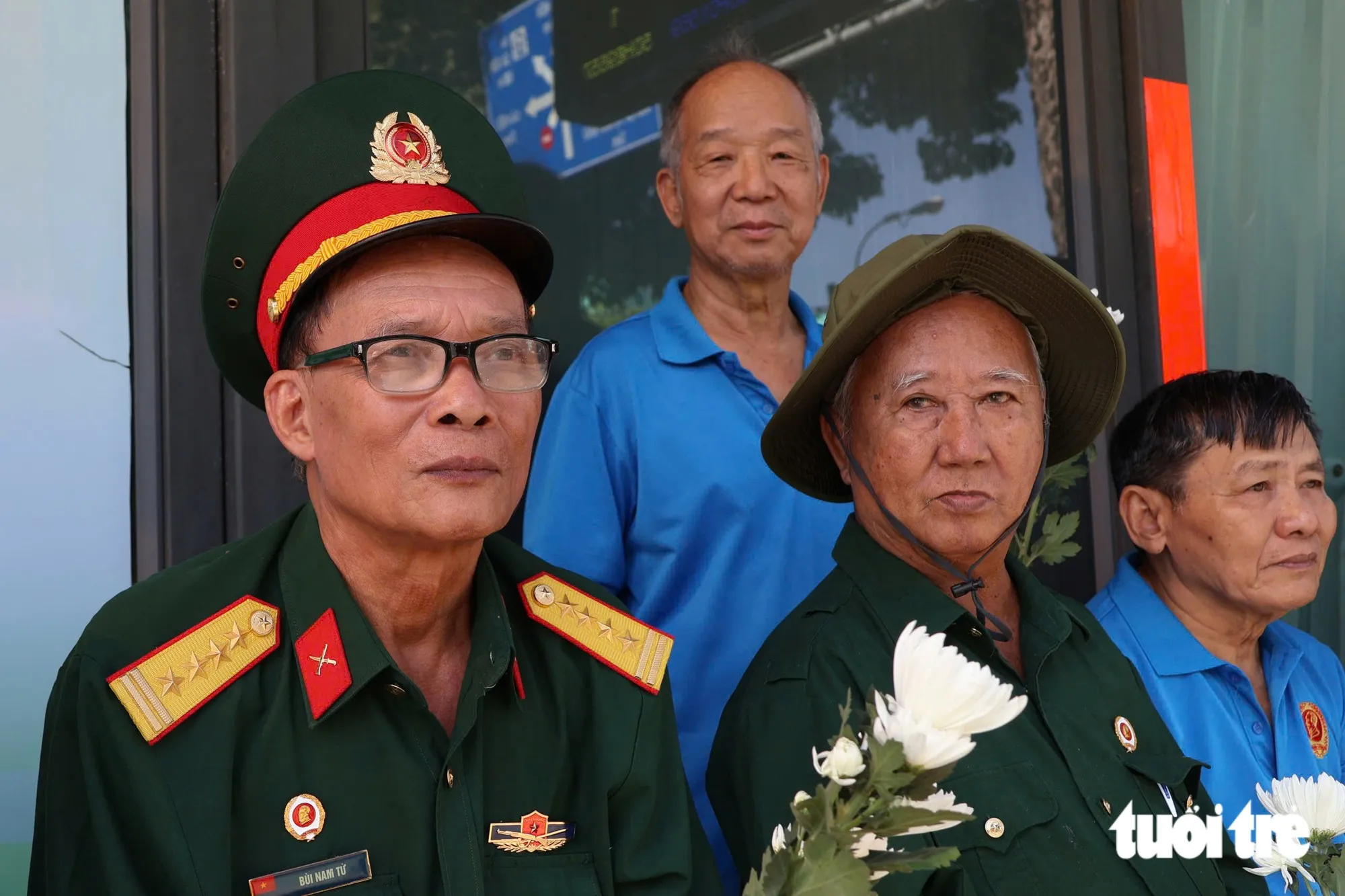 Ông Bùi Nam Từ (thứ nhất từ trái sang), cựu Chủ tịch Hội cựu chiến binh quận 3 (cũ), từng là chiến sĩ tham gia lái xe trên tuyến đường mòn Trường Sơn. Dù năm nay đã 74 tuổi nhưng từ sáng sớm ông đã có mặt tại Vòng xoay Dân chủ để đưa tiễn những người đồng đội.Khi đoàn xe đi qua, ông nghẹn ngào nói: “Tôi thấy thương những người đồng đội của mình lắm, những người đã ngã xuống, đánh đổi sự hi sinh để đem lại hòa bình cho tổ quốc. Tôi thương các đồng đội đã ngã xuống hơn 6 thập kỷ hôm nay đã được trở về nhà. Từ tối tôi đã chuẩn bị hoa và quần áo tươm tất để đến đây tiễn đưa họ về với đất mẹ”, ông Từ xúc động - Ảnh: ĐẶNG LINH