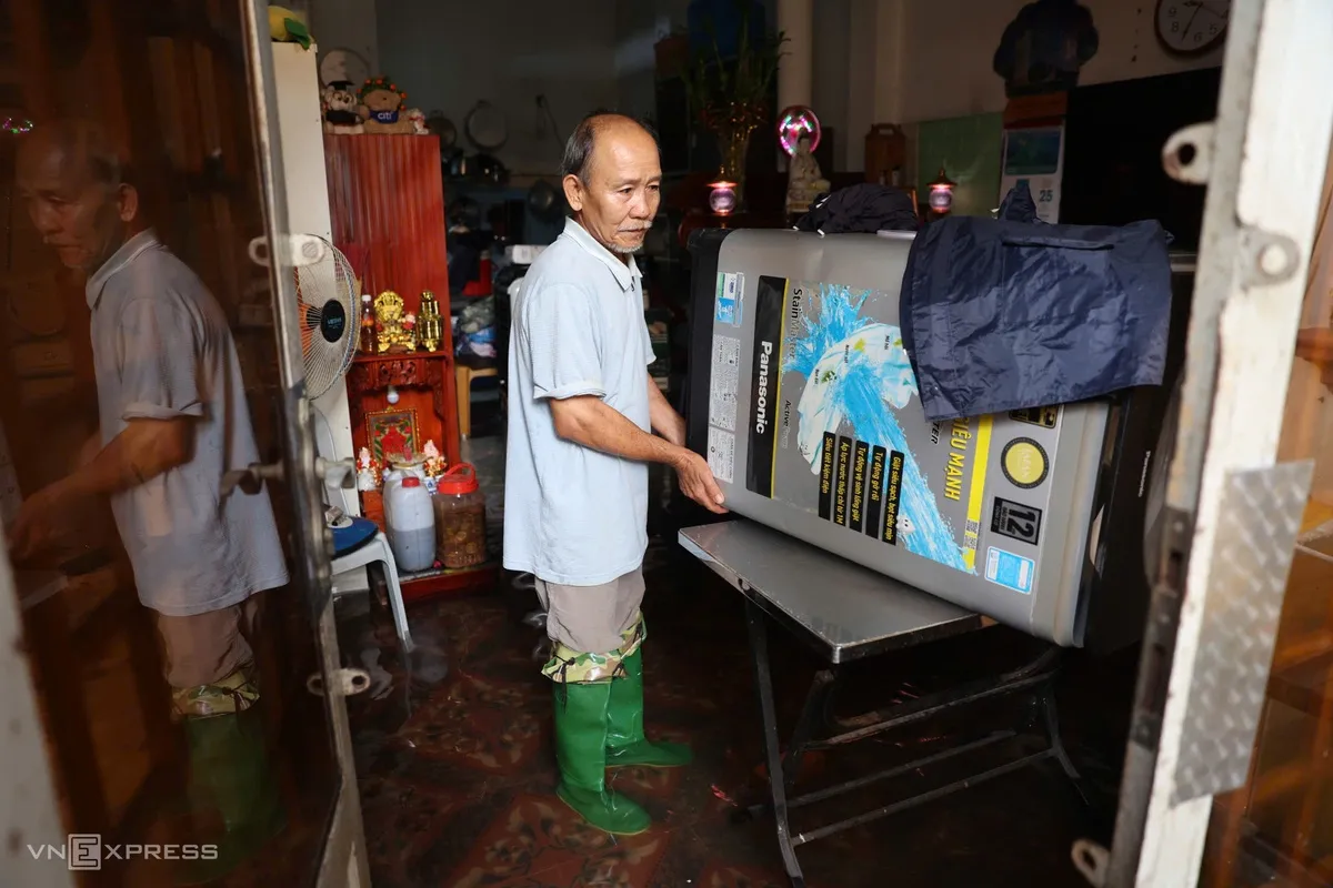 Trong căn nhà ở hẻm 19 đường Quang Trung, ông Văn Minh kê máy giặt lên bàn để tránh nước. Ông cho biết mưa kéo dài suốt đêm, cả gia đình phải ngủ tạm trên ghế sofa.
