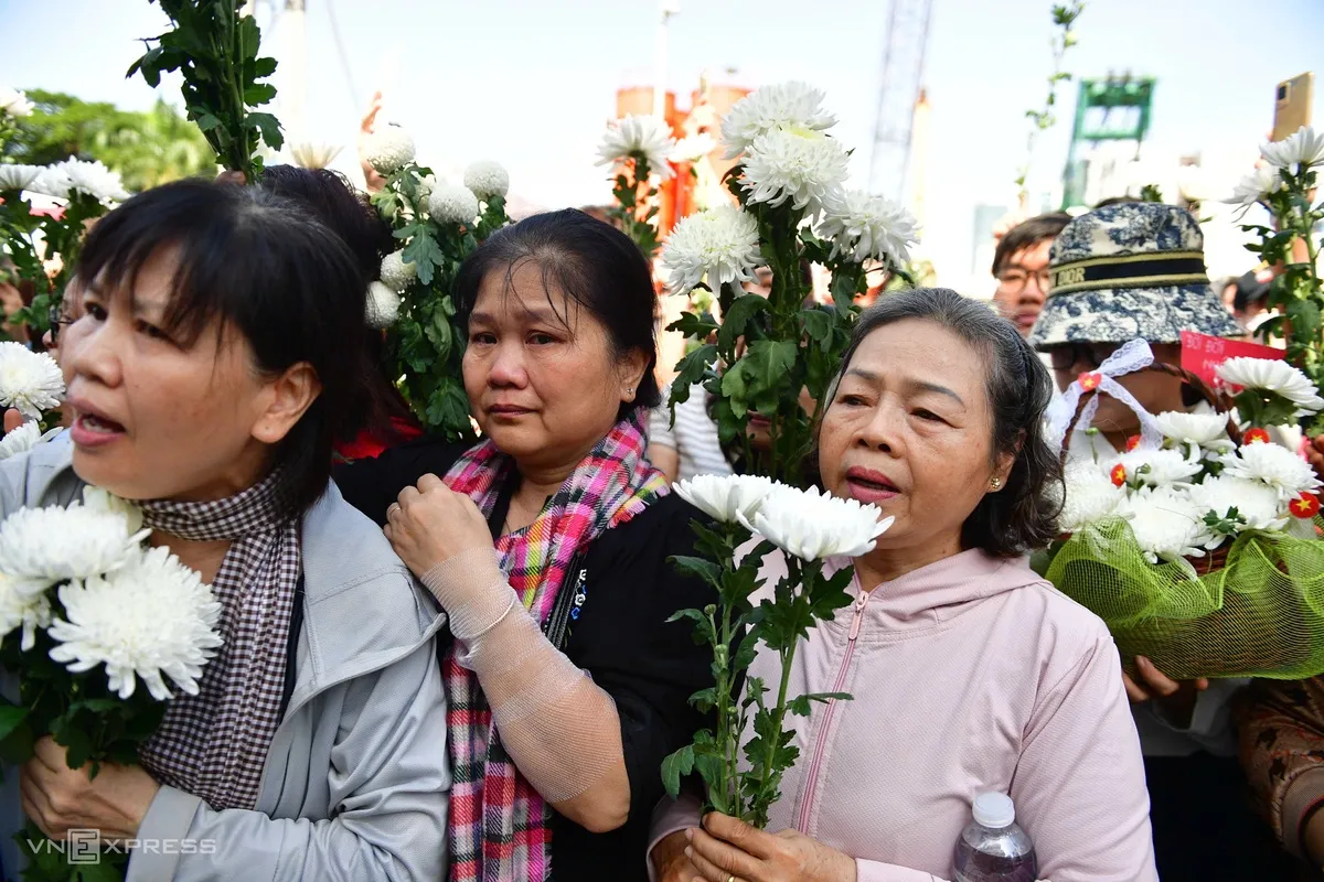 Cờ, hoa trên tay người dân chờ đoàn xe đi qua.
Thảo Phương, 23 tuổi, làm việc tại TP HCM, có mặt từ sáng sớm trên đường Điện Biên Phủ. Cô cùng đồng nghiệp xin phép tạm nghỉ làm để tiễn các liệt sĩ.
