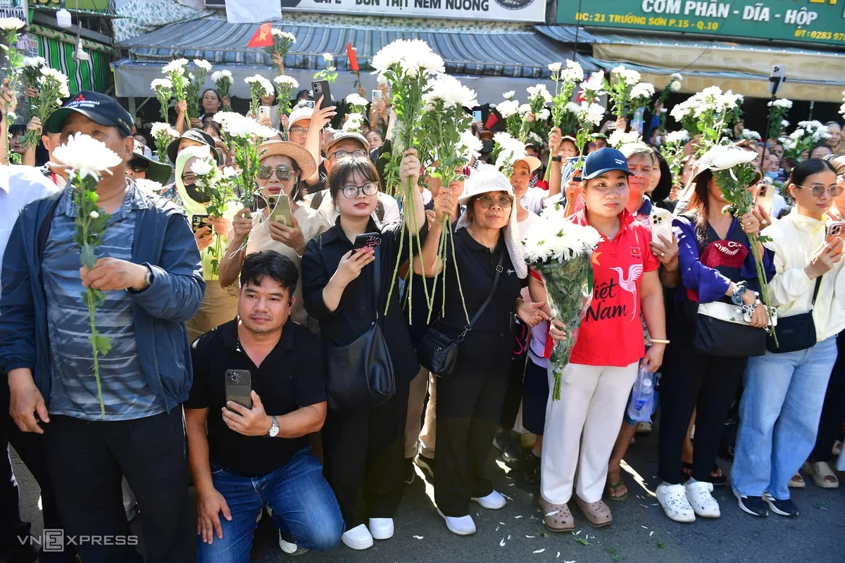Cờ, hoa trên tay người dân chờ đoàn xe đi qua.
Thảo Phương, 23 tuổi, làm việc tại TP HCM, có mặt từ sáng sớm trên đường Điện Biên Phủ. Cô cùng đồng nghiệp xin phép tạm nghỉ làm để tiễn các liệt sĩ.
