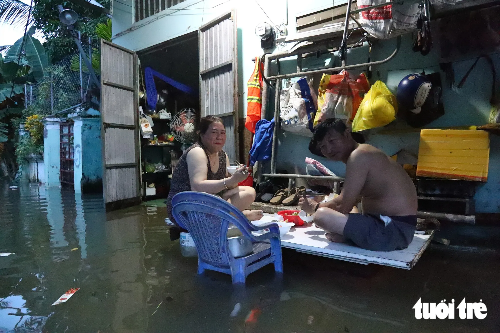 Nước tràn vào nhà, hai vợ chồng sống tại hẻm 142 đường Võ Nguyên Giáp phải kê thùng, lót tấm thép làm chỗ ngồi ăn cơm tối - Ảnh: NGỌC LÂN