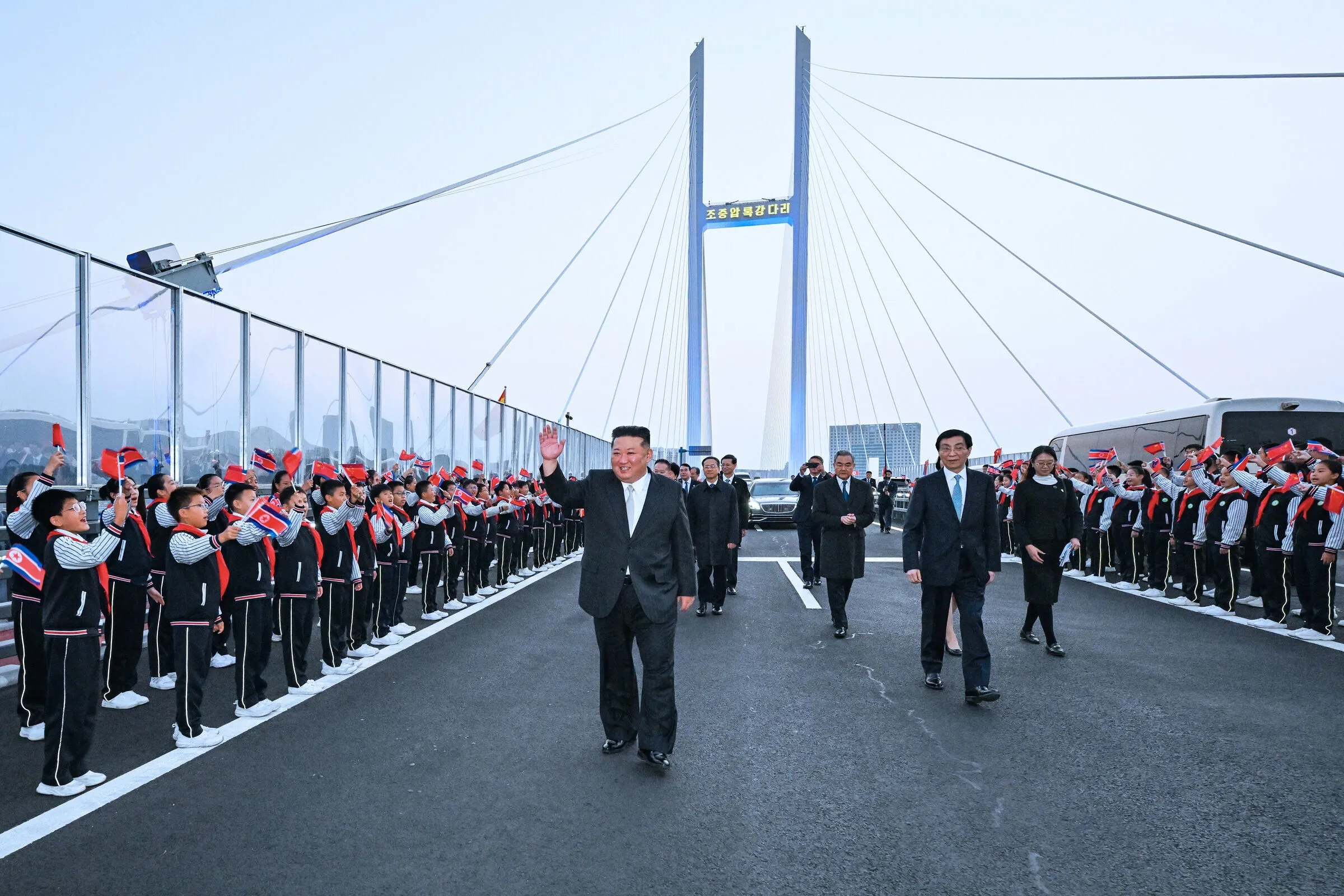 Ông Kim Jong-un cùng ông Vương Hộ Ninh (phải) và các quan chức hai nước đi trên cây cầu mới bắc qua sông Áp Lục, nối Triều Tiên với Đan Đông, Trung Quốc ngày 24/10.