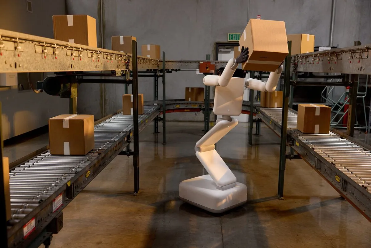 Robot Eno do công ty Genesis AI (Pháp) phát triển, với tay lấy thùng hàng trên băng chuyền tại một nhà kho ở California (Mỹ), ngày 9-6 - Ảnh: REUTERS