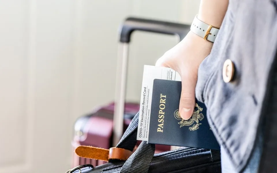 traveler-holding-passport-vaccination-card-luggage-79516979696021069830464-33741826367097429739358.webp